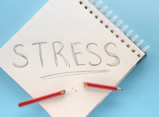 Un carnet à spirale avec le mot "STRESS" écrit en grandes lettres, accompagné d'un crayon rouge cassé, symbolisant le stress et la tension.