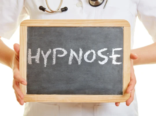 Un professionnel de la santé en blouse blanche tenant un tableau noir avec le mot 'HYPNOSE' écrit en lettres blanches. Qu'est ce que l'hypnose