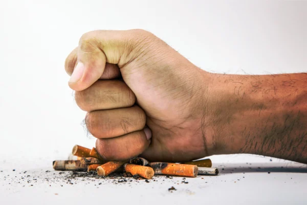 Main fermée en poing écrasant des mégots de cigarettes, symbolisant l'arrêt du tabac et la libération de la dépendance grâce à l'hypnose.